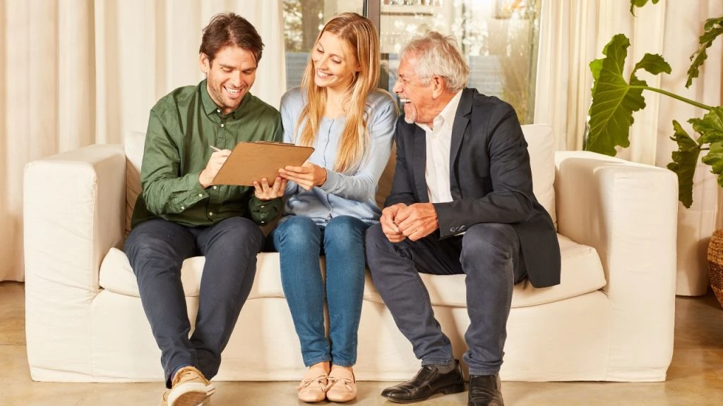 A couple and their property manager sitting on a couch looking at a document