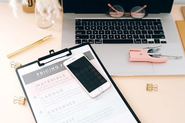 A desk set up with a laptop and clipboard with a pricing structure on it