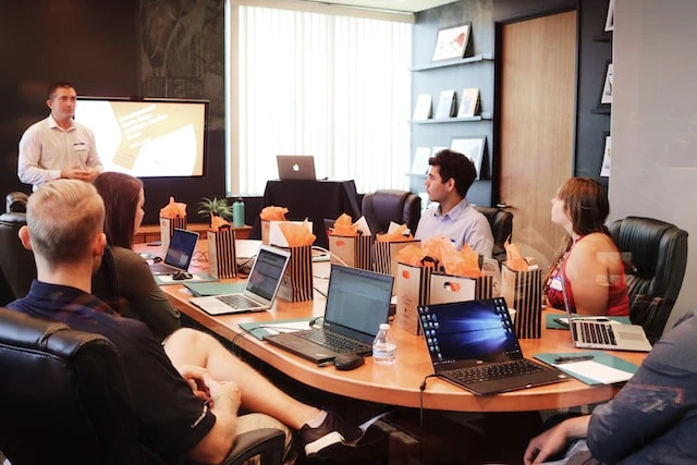 An office of real estate agents around a conference table and someone standing at the front doing a presentation