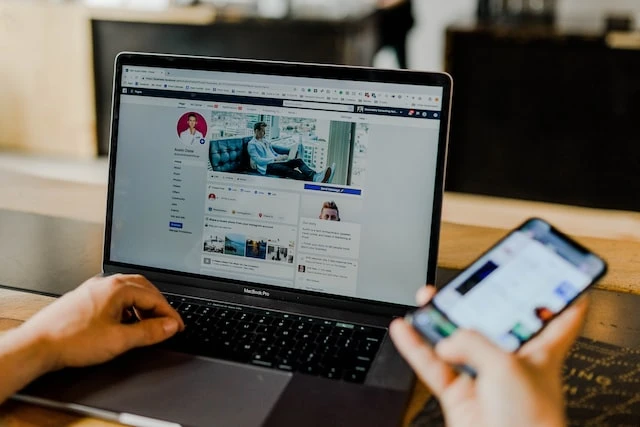 A property manager’s hands holding a smartphone and scrolling through Facebook on a laptop