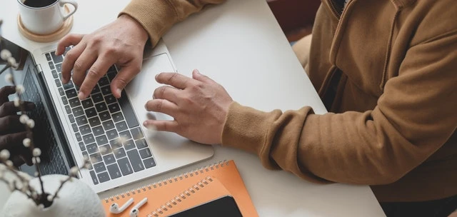 close up of a person sitting at a table using a laptop and online rent payment system
