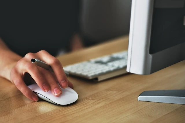 Cropped image of a person’s hand holding a pen while using a white computer mouse
