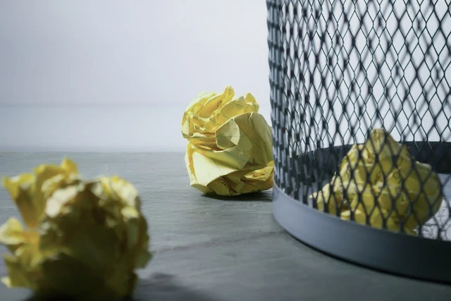 Cropped image of a metal trash bin with crumpled yellow paper around it