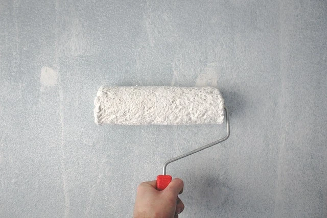Cropped image of a white paint roller on a grey wall
