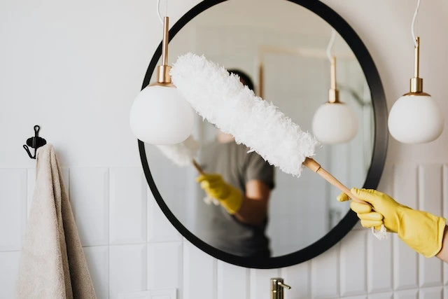 Cropped image of someone wearing yellow cleaning gloves cleaning a ceiling light with a feather duster