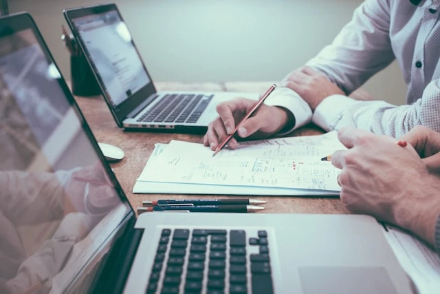 Cropped image of two people working next to each other with laptops and notes