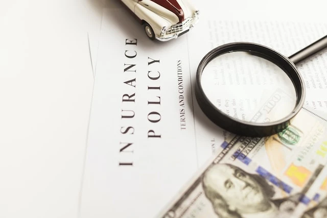 Document with Insurance Policy printed on it, a 100 dollar bill and magnifying glass are on top of the paper