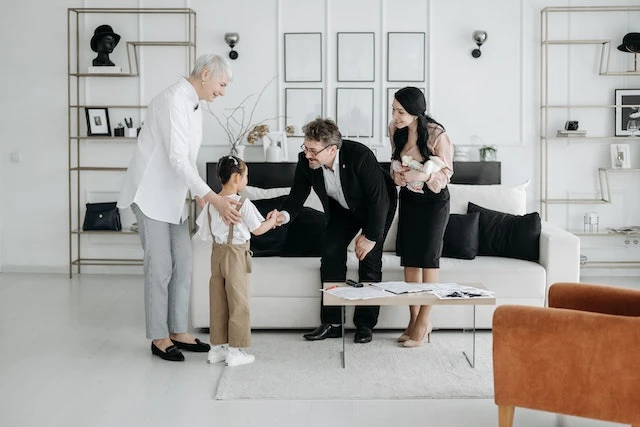 Four people in a living room, one adult is shaking a child’s hand