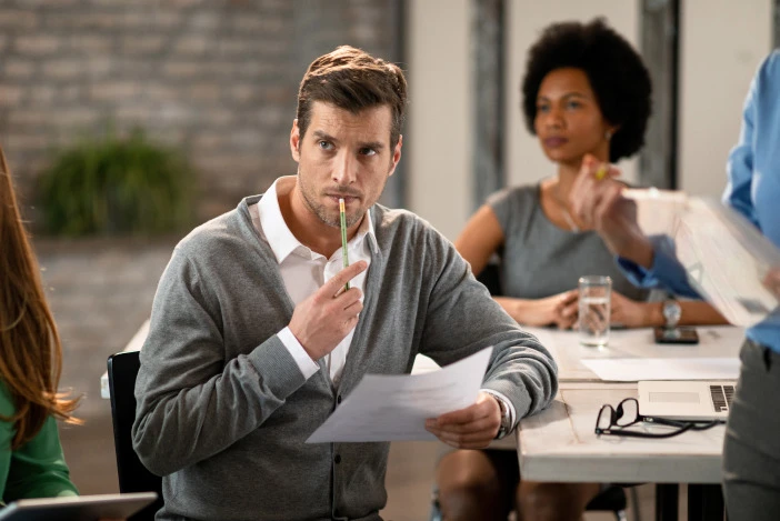 Property manager reviewing paperwork with a thoughtful, concerned expression during a team meeting