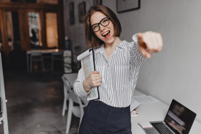 Ecstatic woman in a button up shirt pointing at the camera