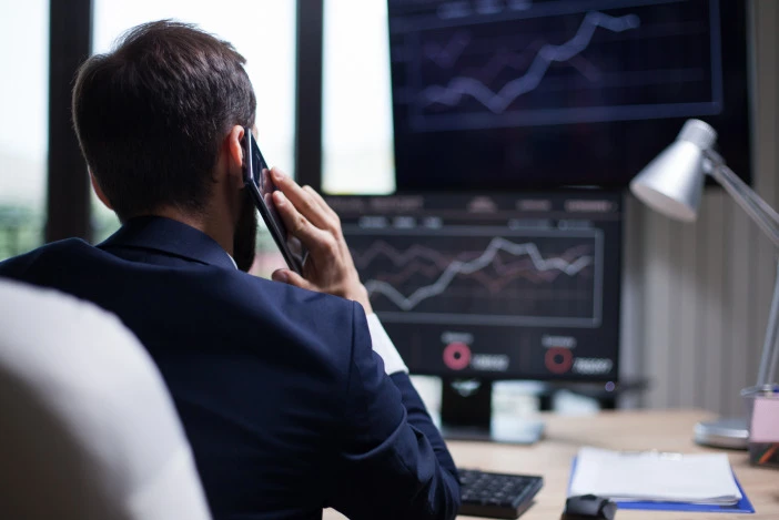 Professional on the phone reviewing market charts on dual monitors