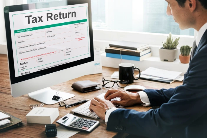 Man in a suit working at his desk on his Tax Return on the desktop computer in front of him