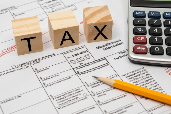 Tax documents with a pencil, calculator, and three wood blocks spelling out “TAX”