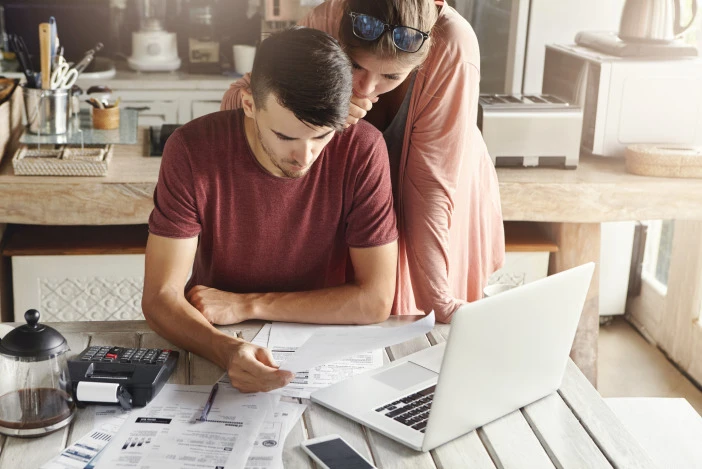 Two people looking at a computer and documents at a desk together