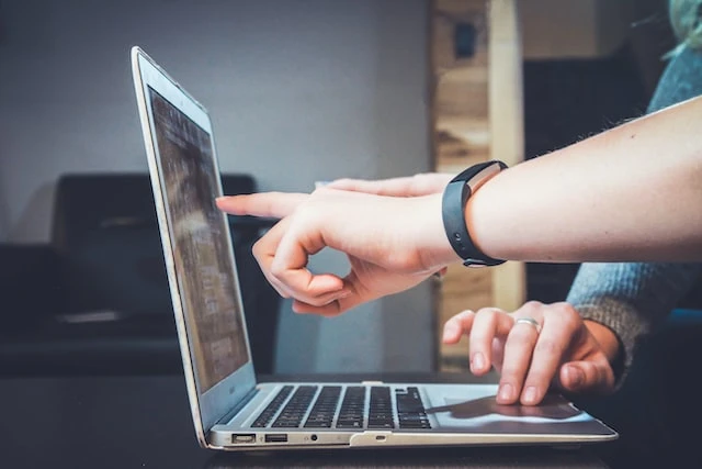 One person pointing at a laptop screen while another person types on the keyboard