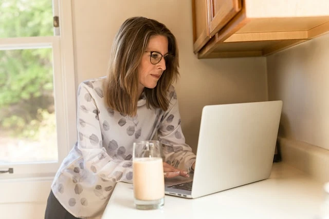 Person in glasses looking at their laptop while standing at their kitchen counter