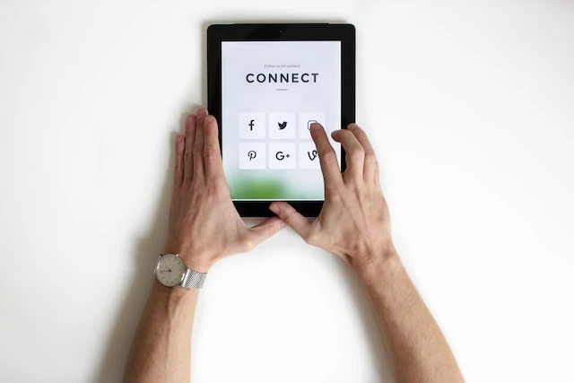 Person’s hands holding a tablet that says “CONNECT” across the top with social media icons