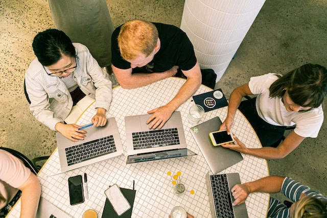 Overhead shot of a group of five people sitting around a table working on their laptops