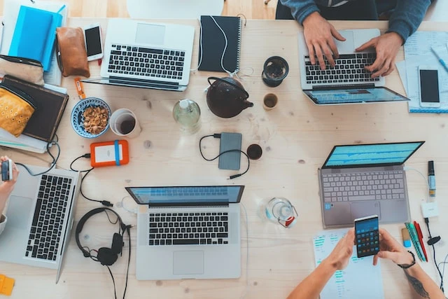 Overhead shot of a table where a group of five people are working on their laptops
