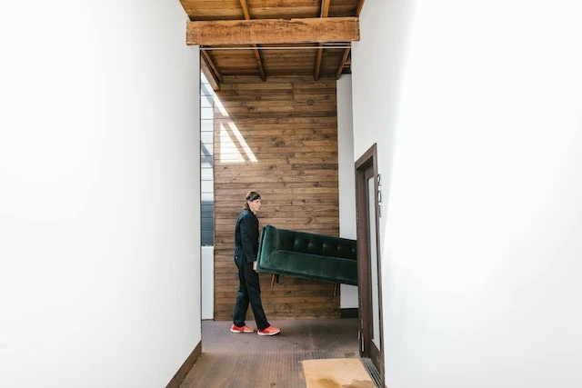 Person holding a green velvet couch walking towards an open doorway