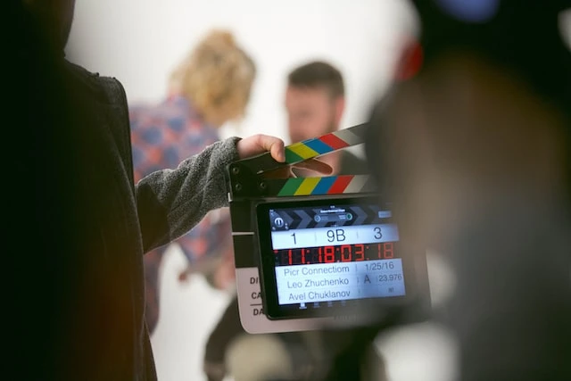 Person in the foreground holding up a film slate in front of two people in the background