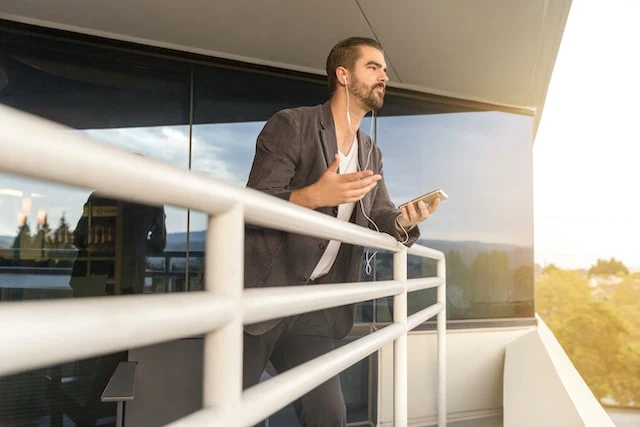 A real estate agent cold calling a lead while leaning against a balcony and wearing white earbuds