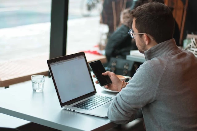 Person sitting at a table working on their laptop and phone