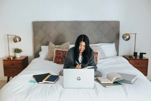 Property manager sitting on a large bed using their laptop and working out of multiple books and notebooks