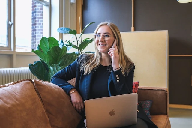 A real estate agent with blonde hair sitting on a leather couch talking on the phone