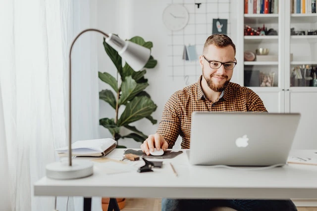 Person with glasses sitting at a desk looking at their laptop
