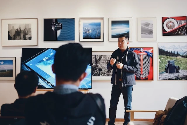 Person standing next to a TV screen giving a talk to a room of people