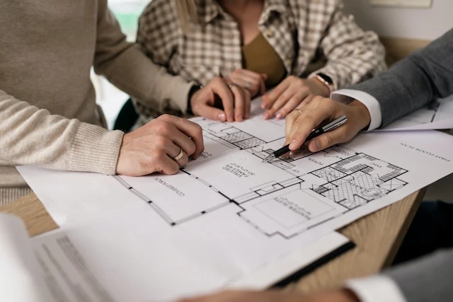 Three people’s hands over a drawing of a house’s layout