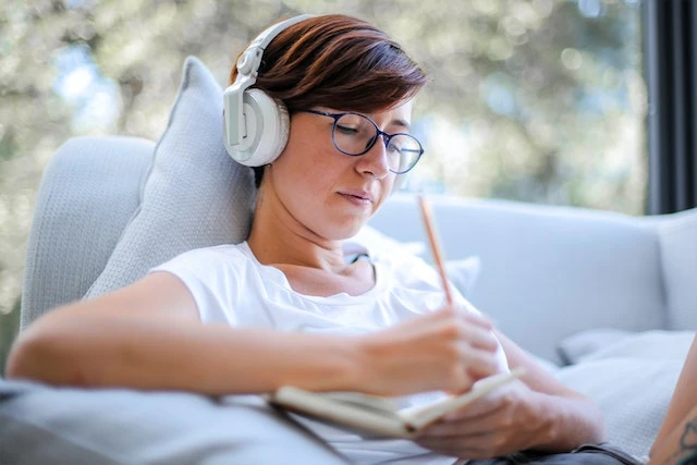 Person wearing headphones, sitting on a couch and taking notes in a notebook