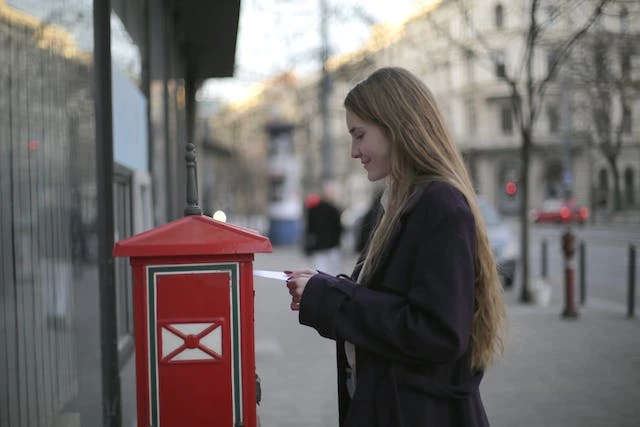 Woman putting a letter in a red mailbox on the street