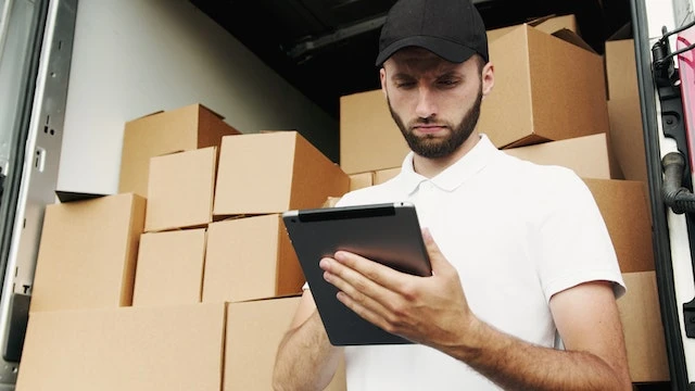 Person standing in front of a moving truck full of cardboard boxes looking at a tablet