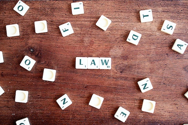 Scrabble letters scattered on a wooden table, three in the middle spell out “law”