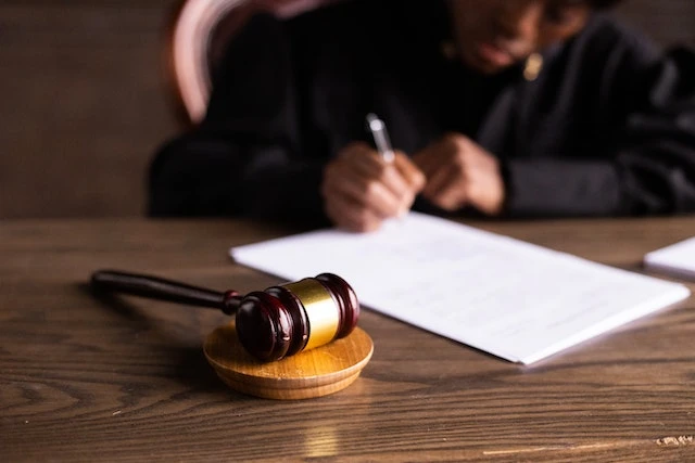 A wooden gavel on a desk in front of a person signing a document