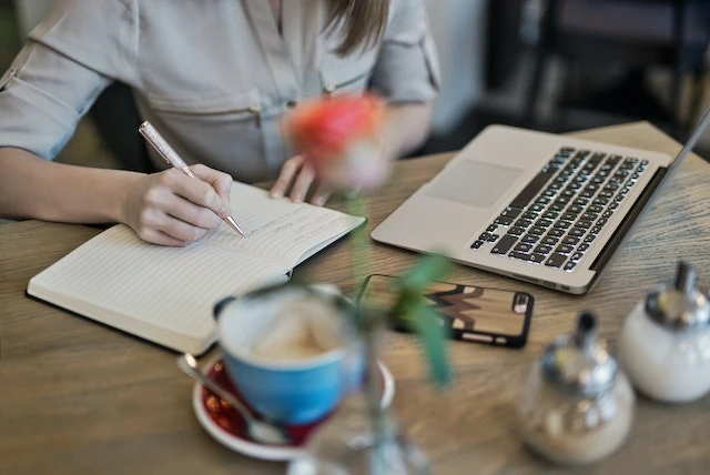 Hands writing in a notebook in front of a laptop