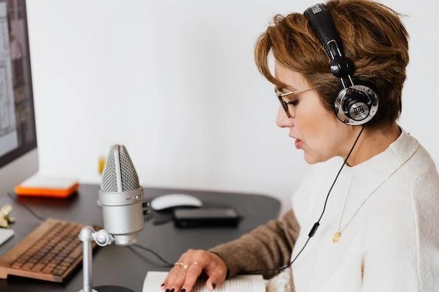 Person in a white shirt recording a podcast with a microphone at their desk