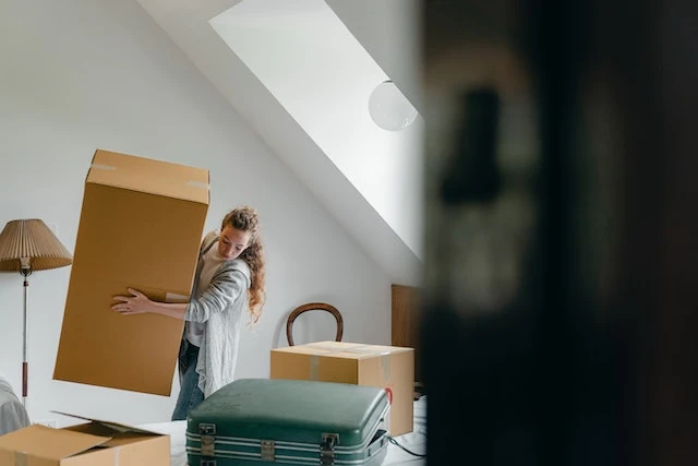 Person holding a large cardboard box in their packed up apartment