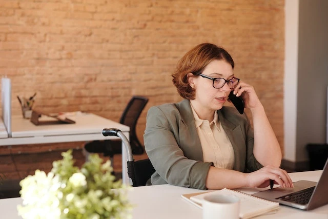 Person speaking on the phone while looking at their laptop at a desk