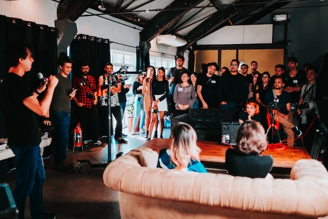 A room full of people, two are sitting on a couch being interviewed while it’s filmed