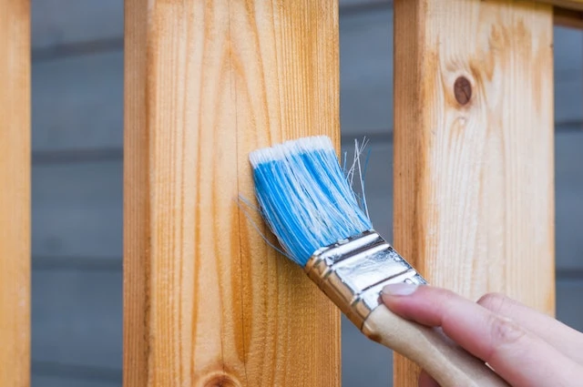 Paintbrush putting wood stain on a wood fence