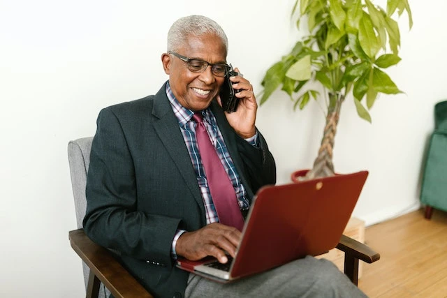 Person in a suit sitting in a chair, talking on a phone with a laptop on their lap