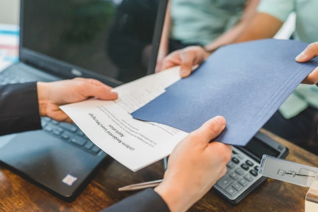 Hands exchanging a folder of papers over a desk
