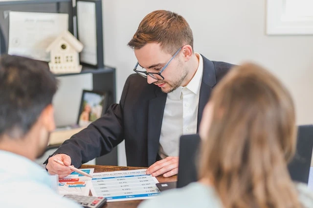 Person looking at documents on their desk and speaking with two people
