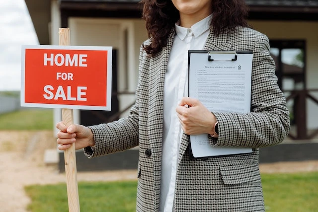Real estate agent standing in front of a house with a small red home for sale sign