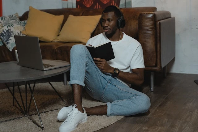 Man sitting on the floor in front of a couch listening to a podcast with headphones while taking notes in a notebook