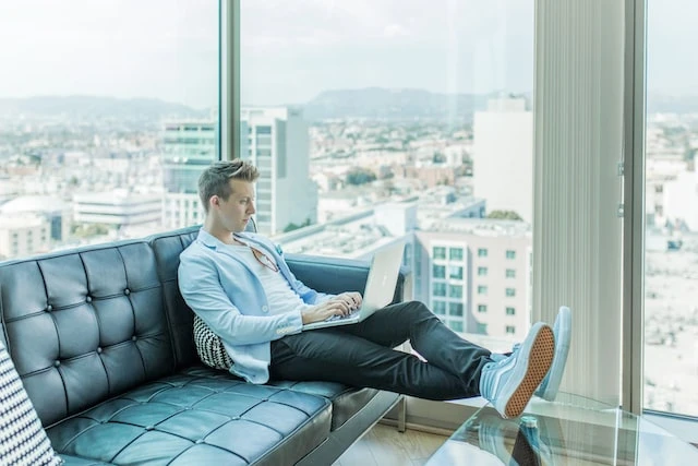 Property manager sitting casually on a couch in an office building working on his laptop