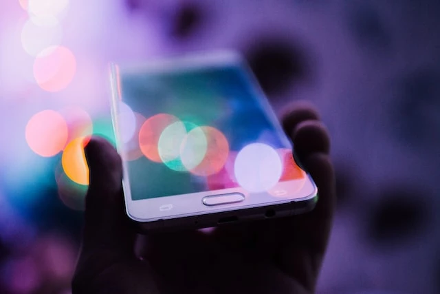 A hand holding a smartphone up with lens flares across the screen